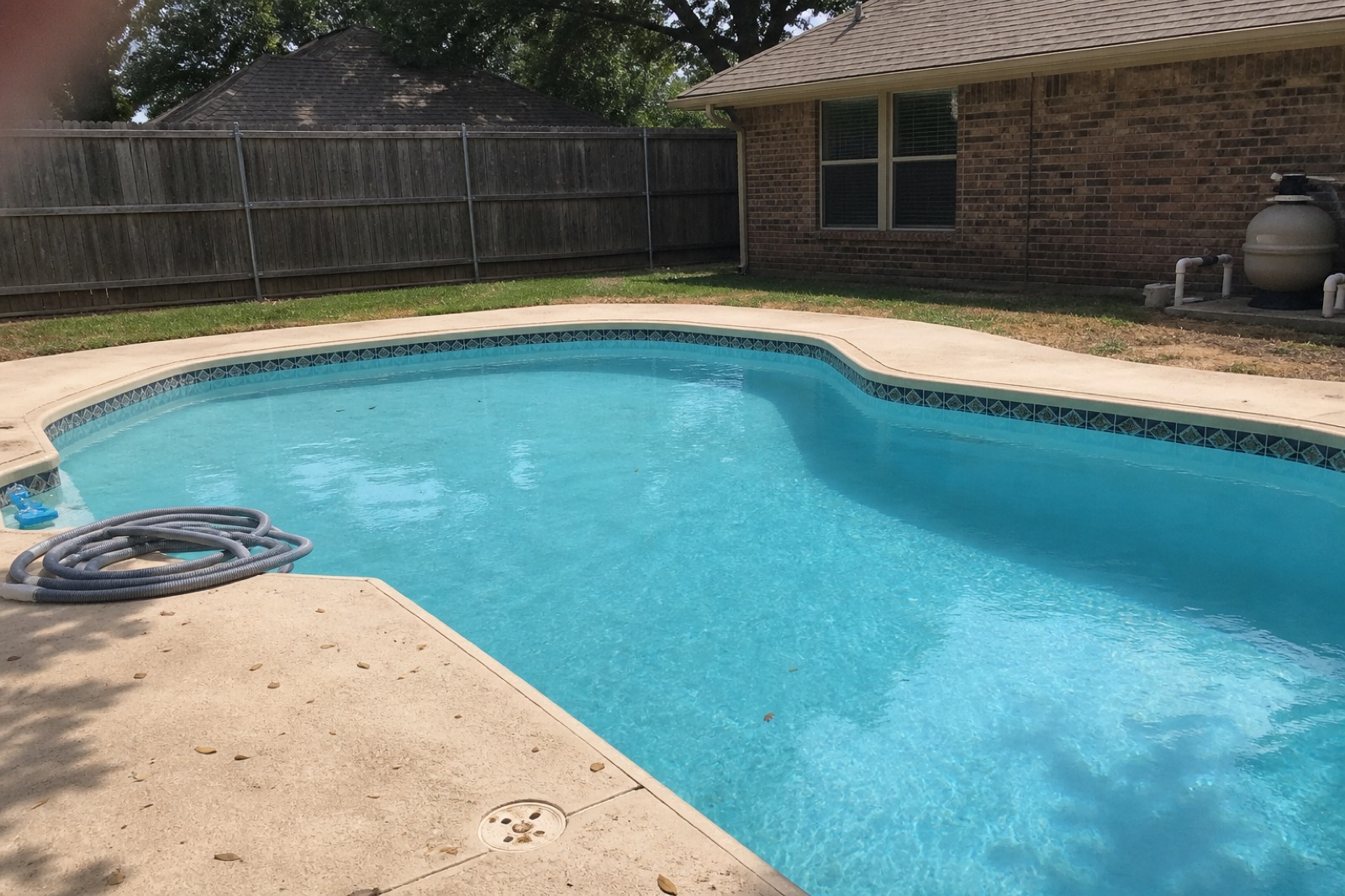 Backyard pool with vacuum hose coiled at the skimmer, equipment pad visible at the far edge.