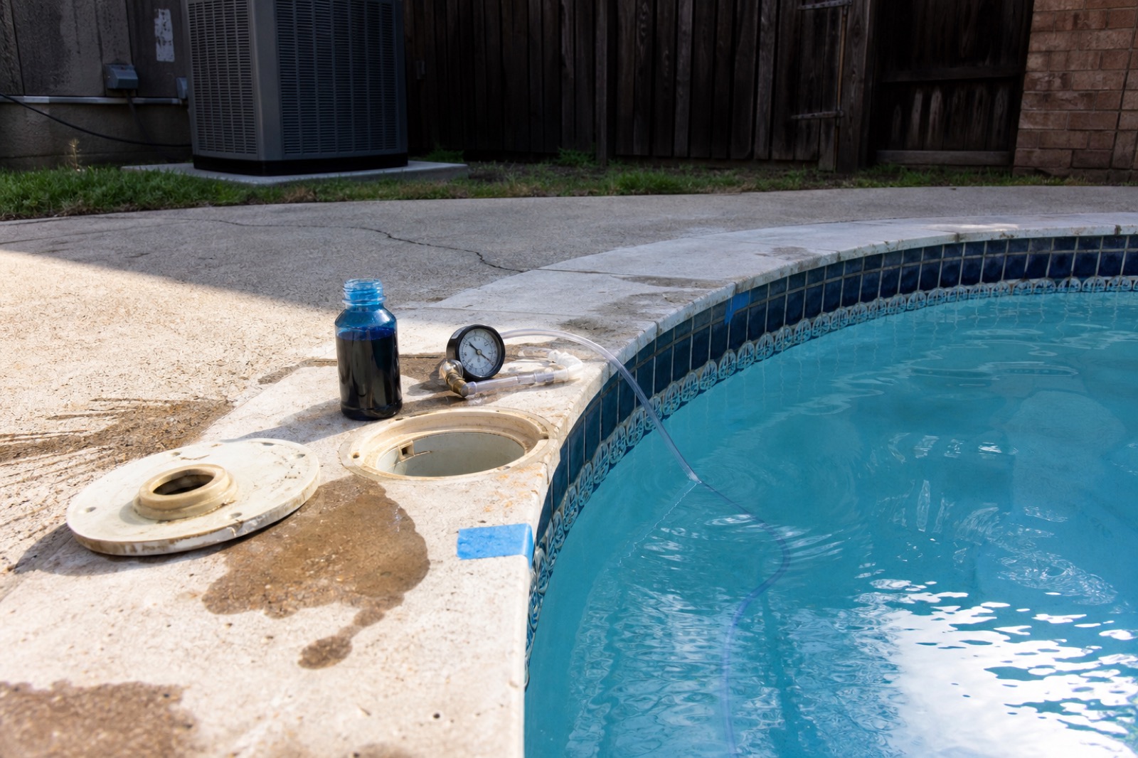 Leak detection in progress — dye test bottle, pressure gauge, and tubing at the skimmer coping.